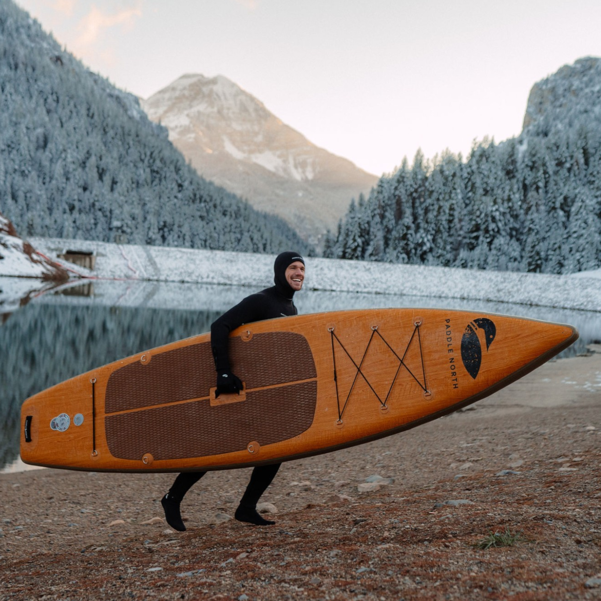 man holding inflatable paddle board while wearing a wet suit