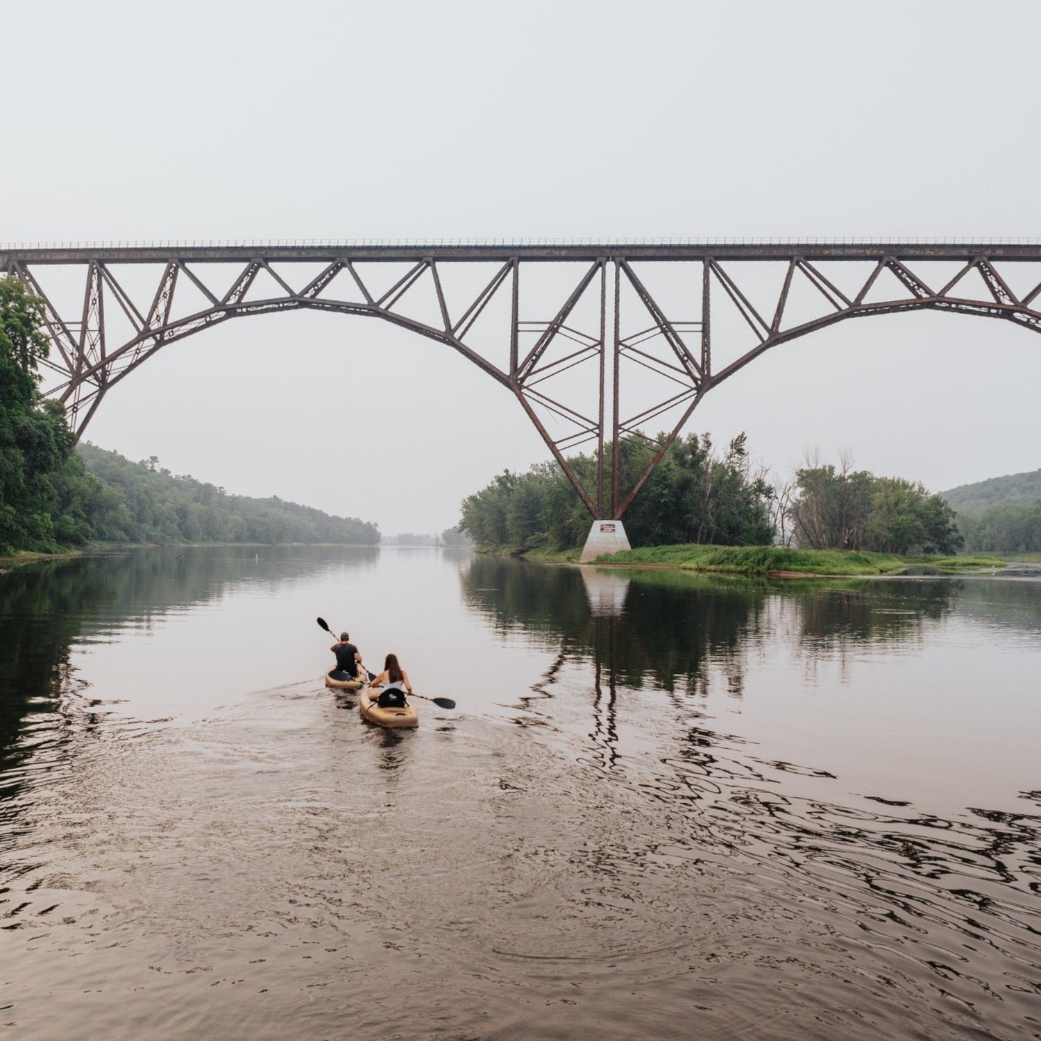 two people kayaking on a river under a bridge paddle north inflatable kayak