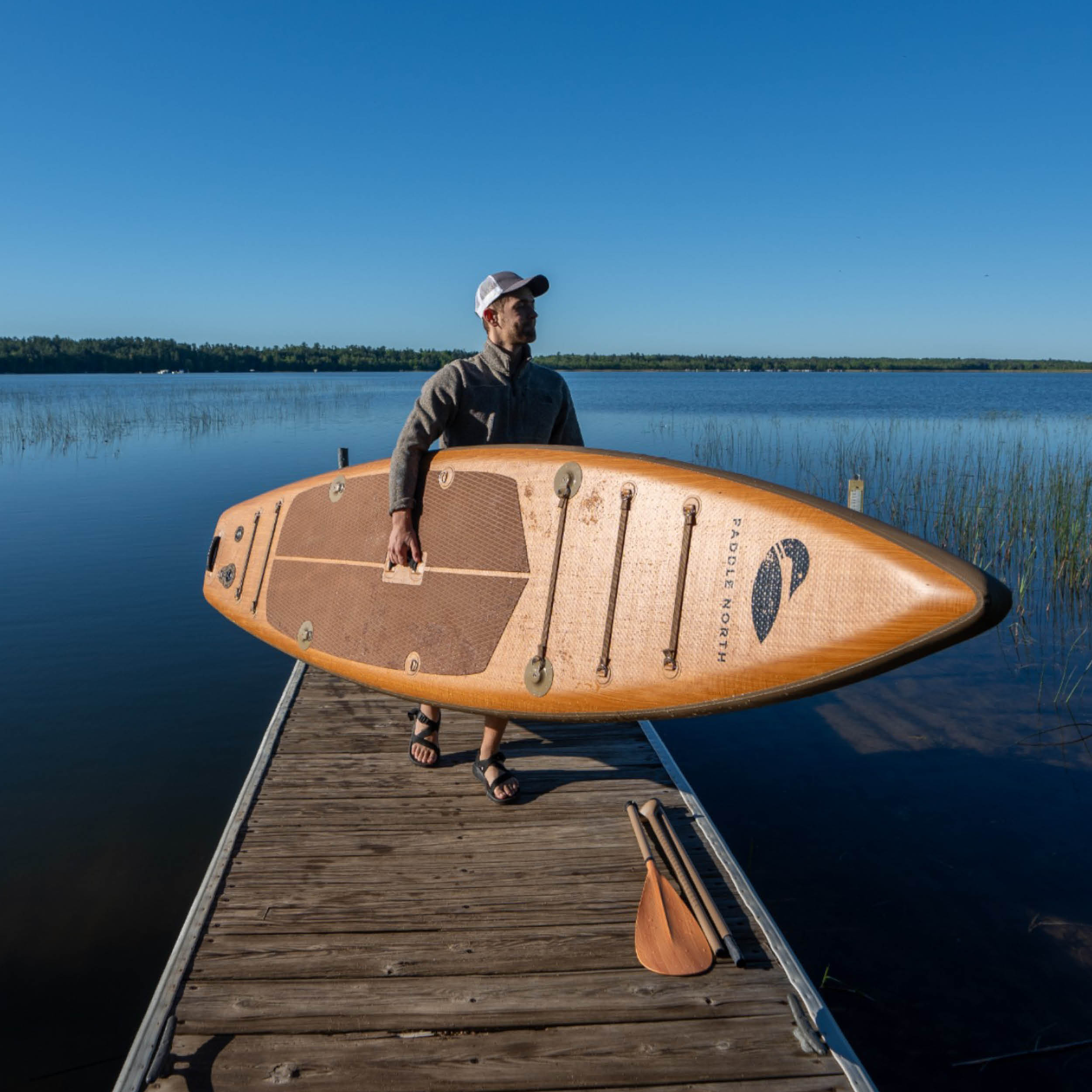 man holding inflatable paddle board on dock at a minnesota lake