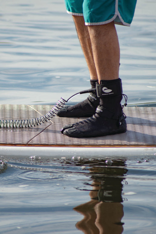 Close up on the 10' SUP leash in use on a stand up paddle board (SUP) showcasing the black anklet on a leg with Paddle North water shoes.