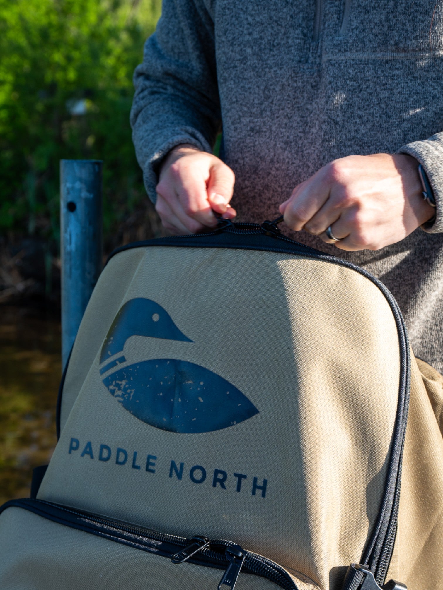 Close up photo of person holding a tan paddle north backpack by the top handle outside.