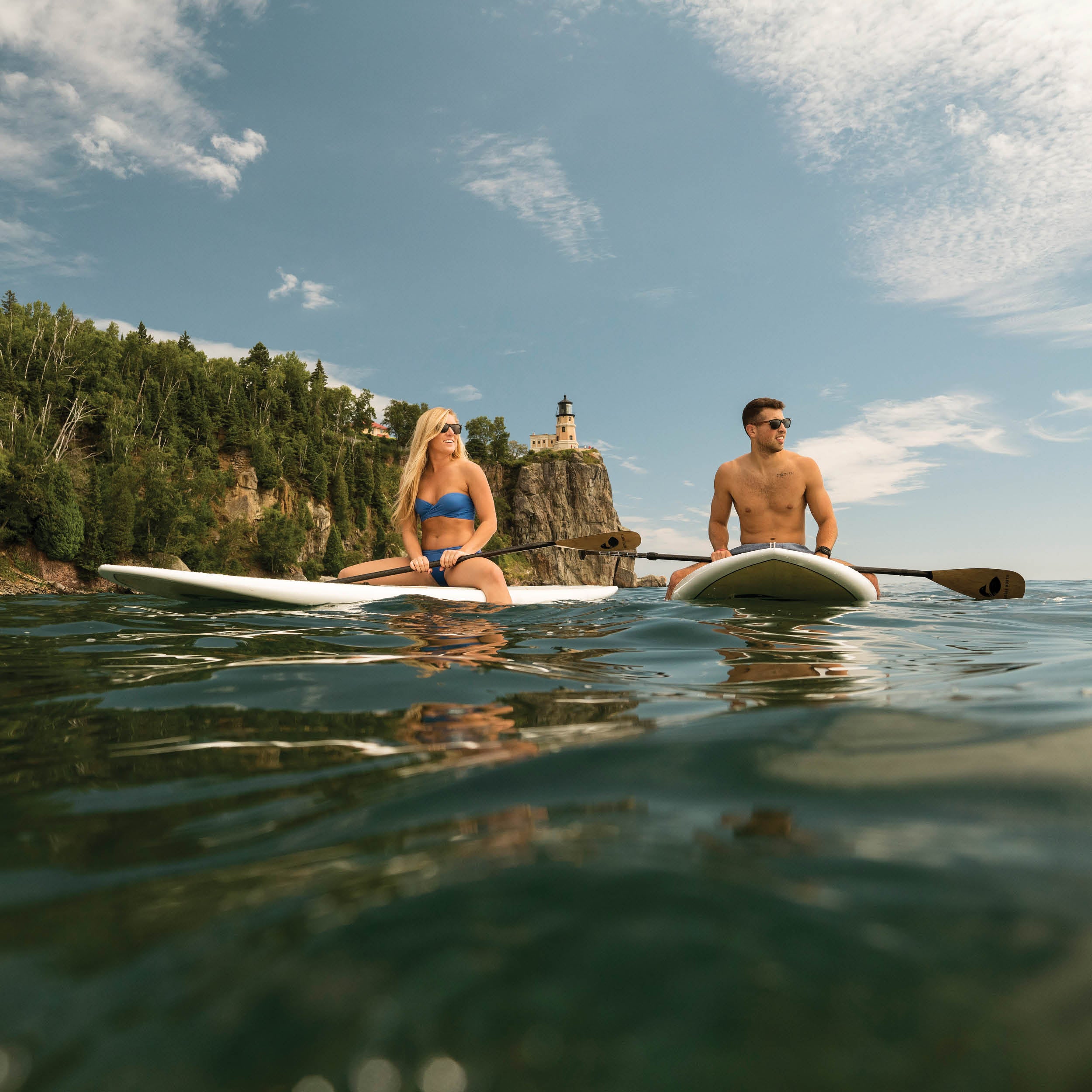 Two people paddle boarding on a lake with two hard paddle board with a scenic background