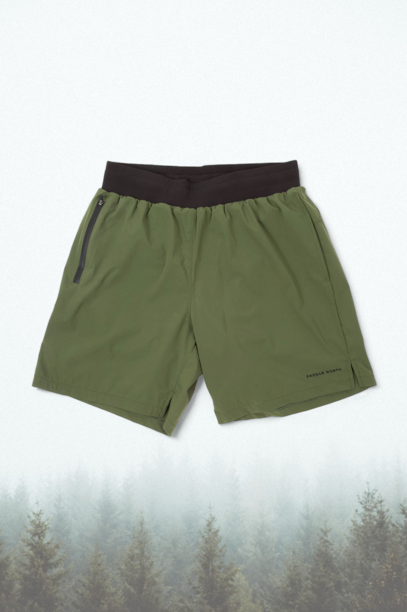 Green shorts with a black elastic waistband against an evergreen tree background.