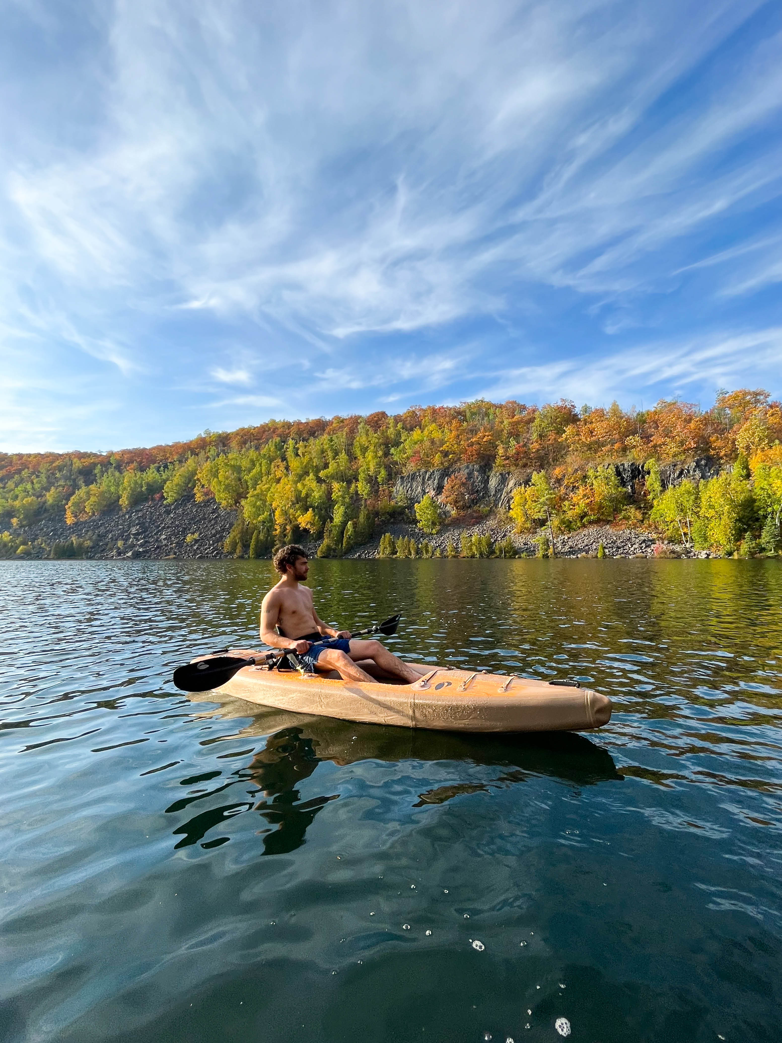 Person kayaking in water with trees in the background.