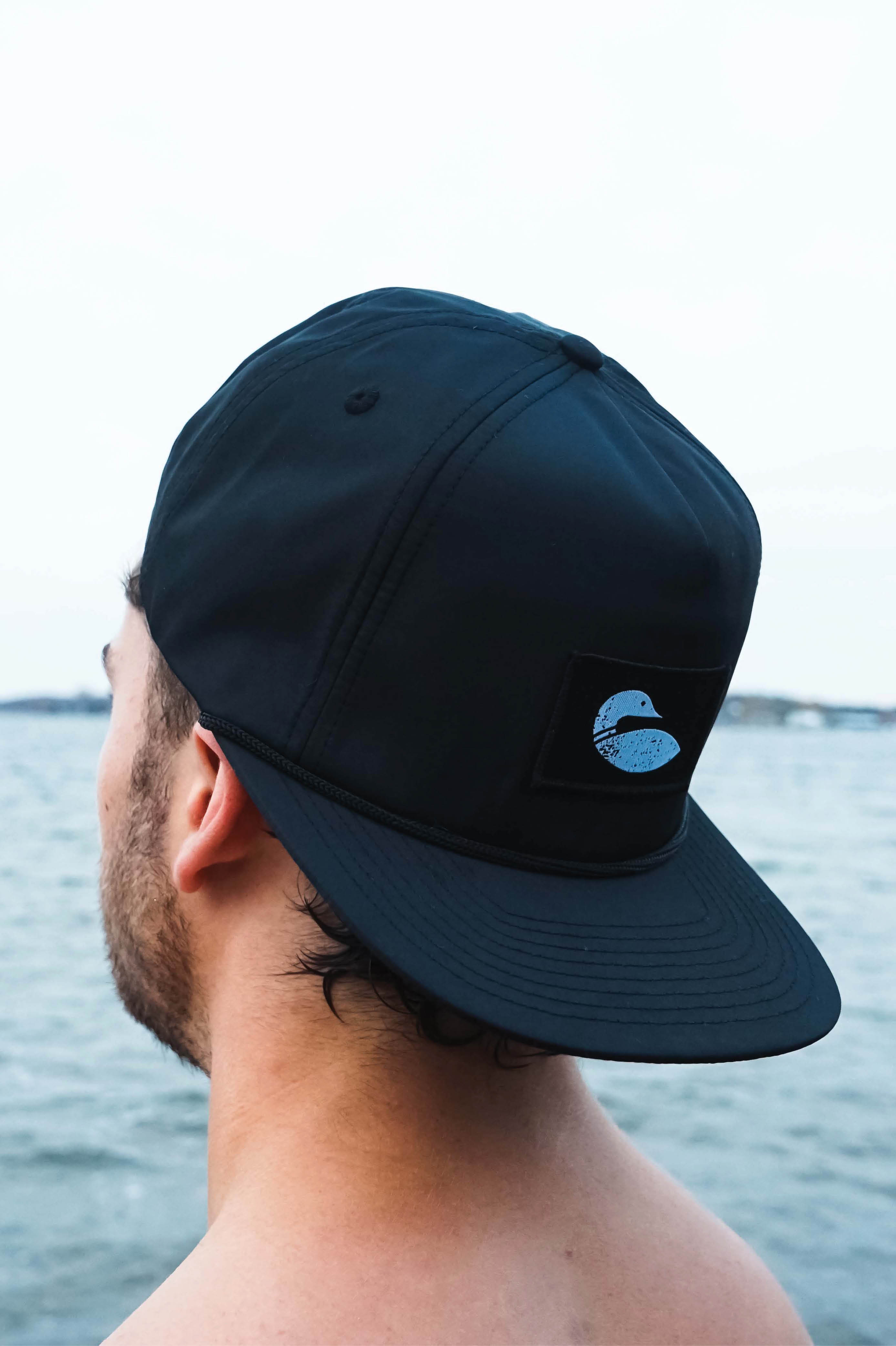 Person wearing black snapback hat backwards showing the loon logo.
