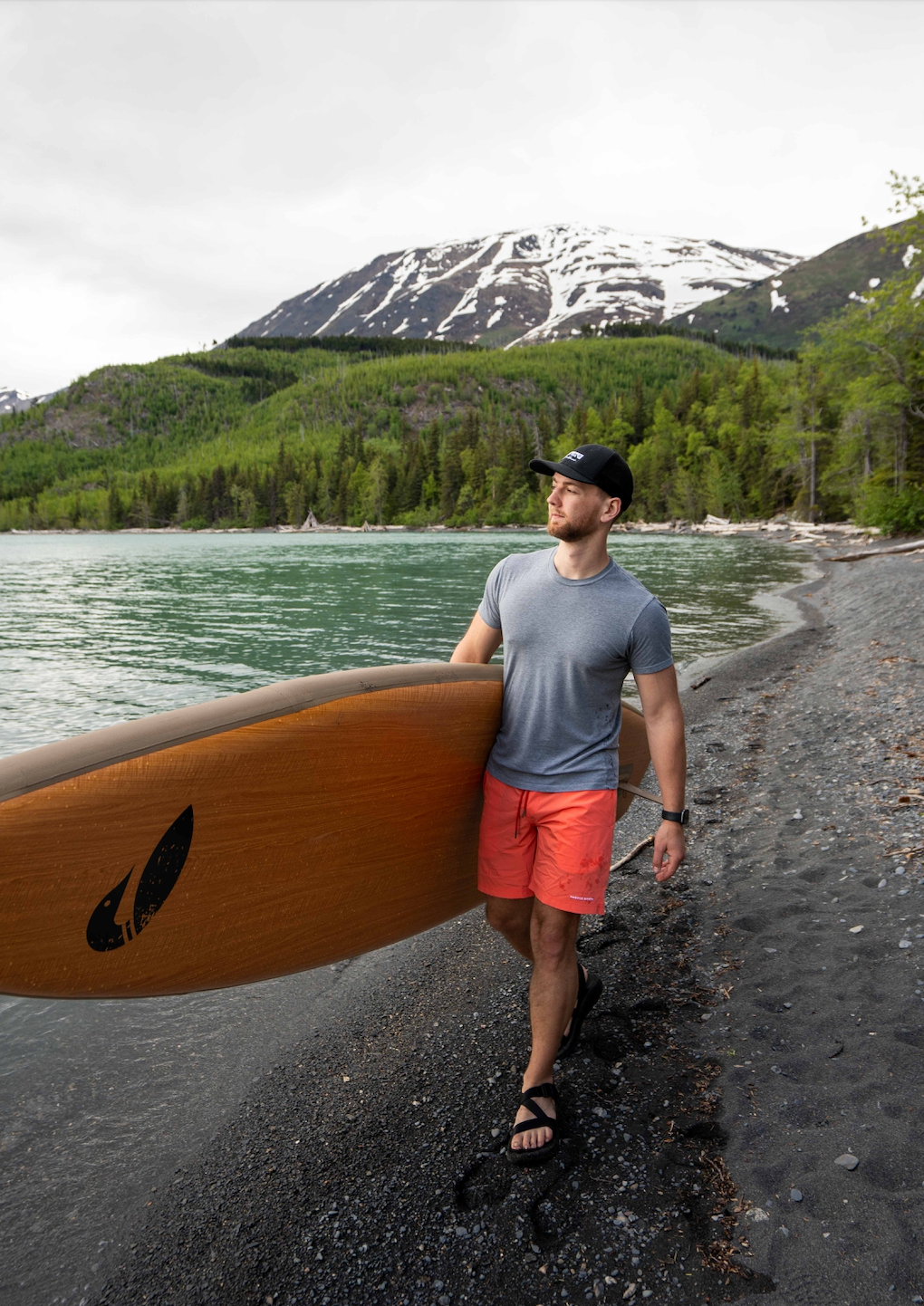 Man carrying inflatable paddle board next to lake with mountains in the background