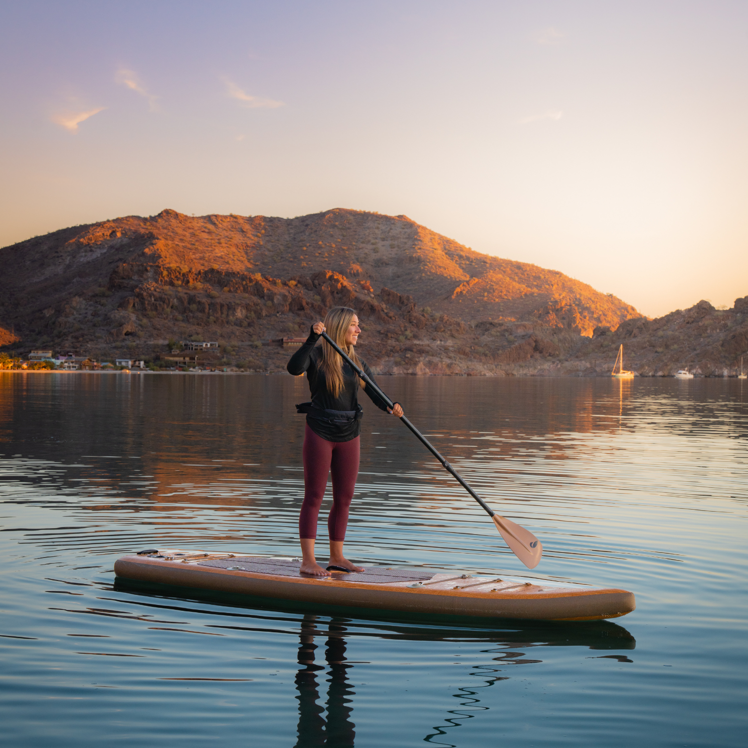 Woman paddle boarding and inflatable paddle board on a lake with mountains in the background during sunset.