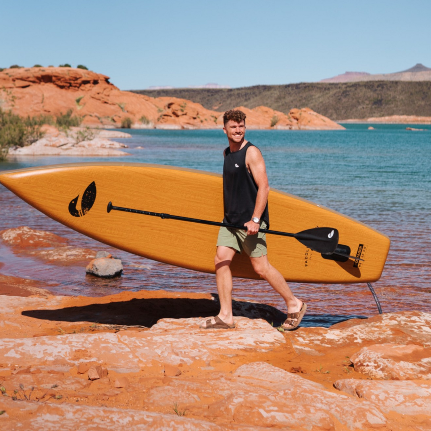 man carrying inflatable paddle board on rocky shoreline
