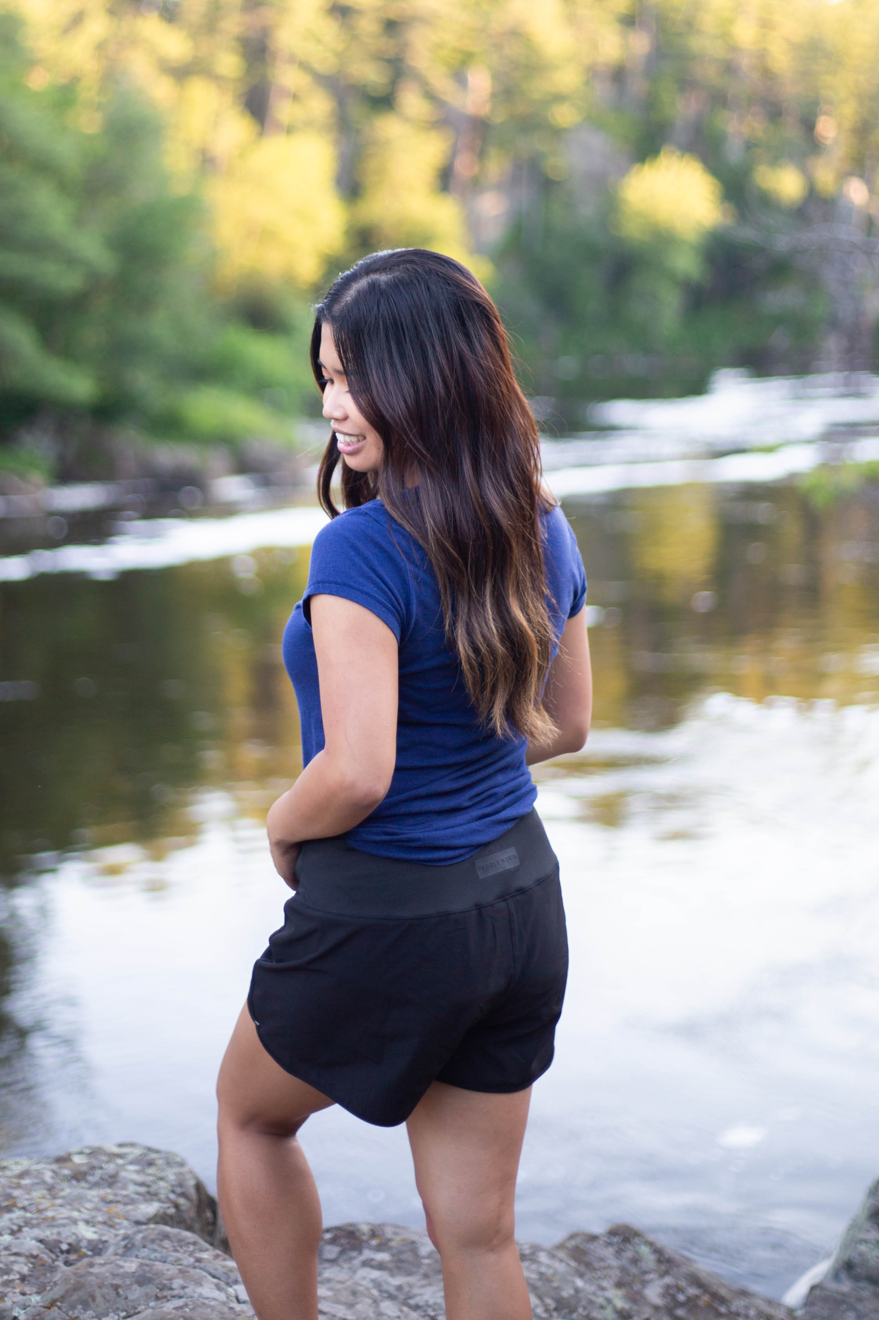 Woman wearing black paddle north shorts by water.