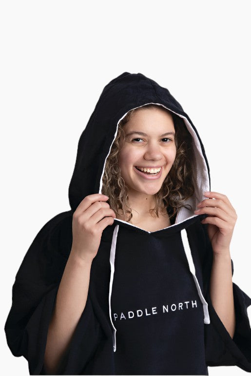 Person wearing a black poncho with white lining smiling with their hood up.