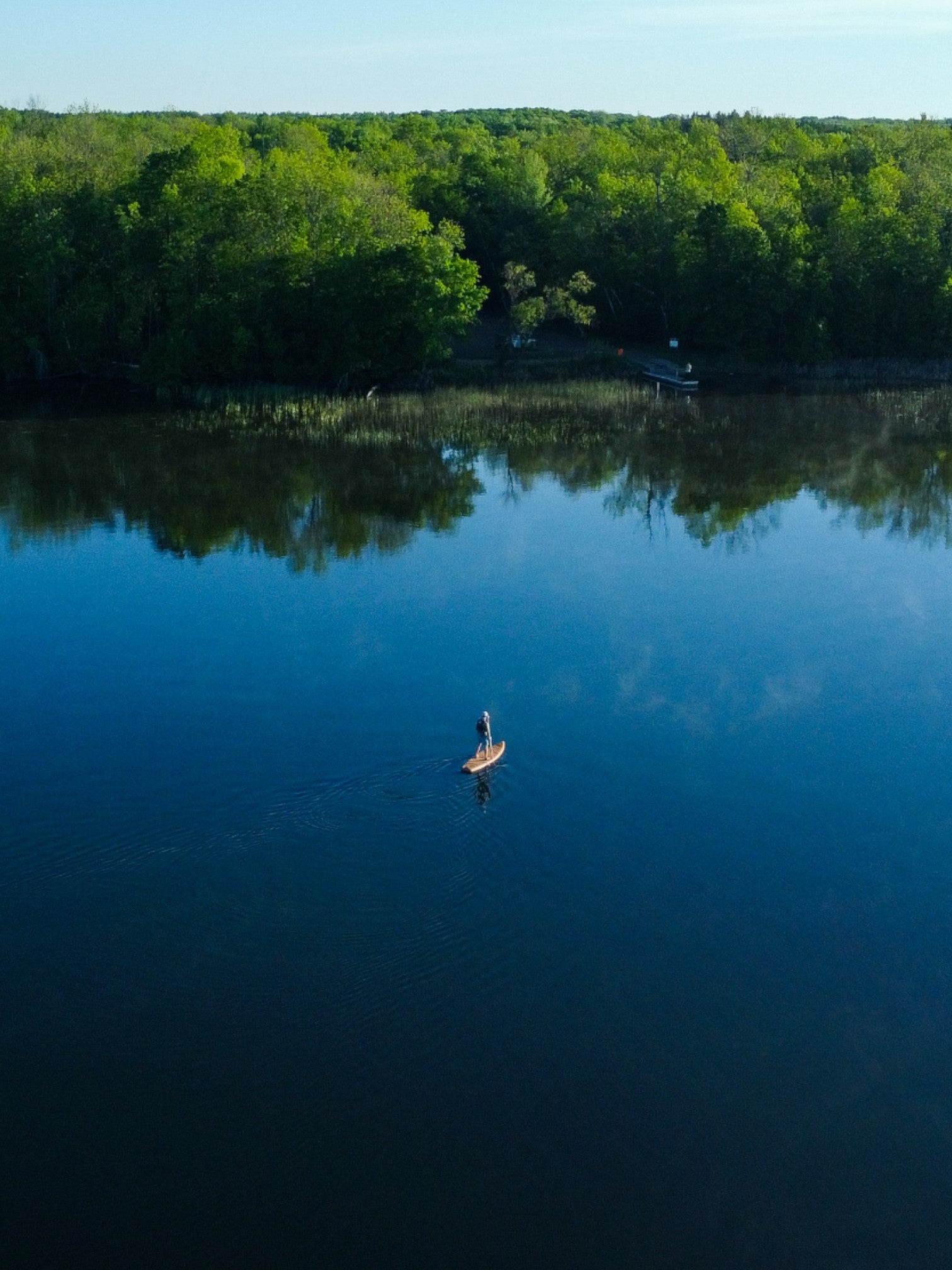 Drone shot of a person paddle boarding on a sunny day surrounded by water.