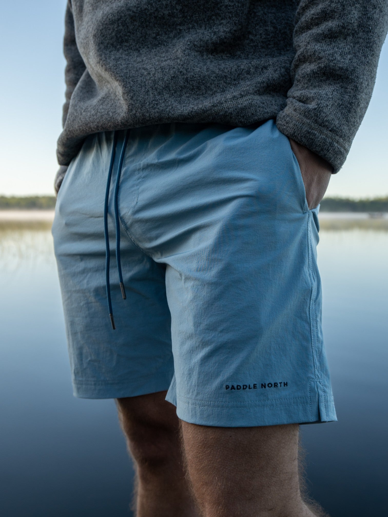 Man wearing blue shorts outside with blue water behind him.