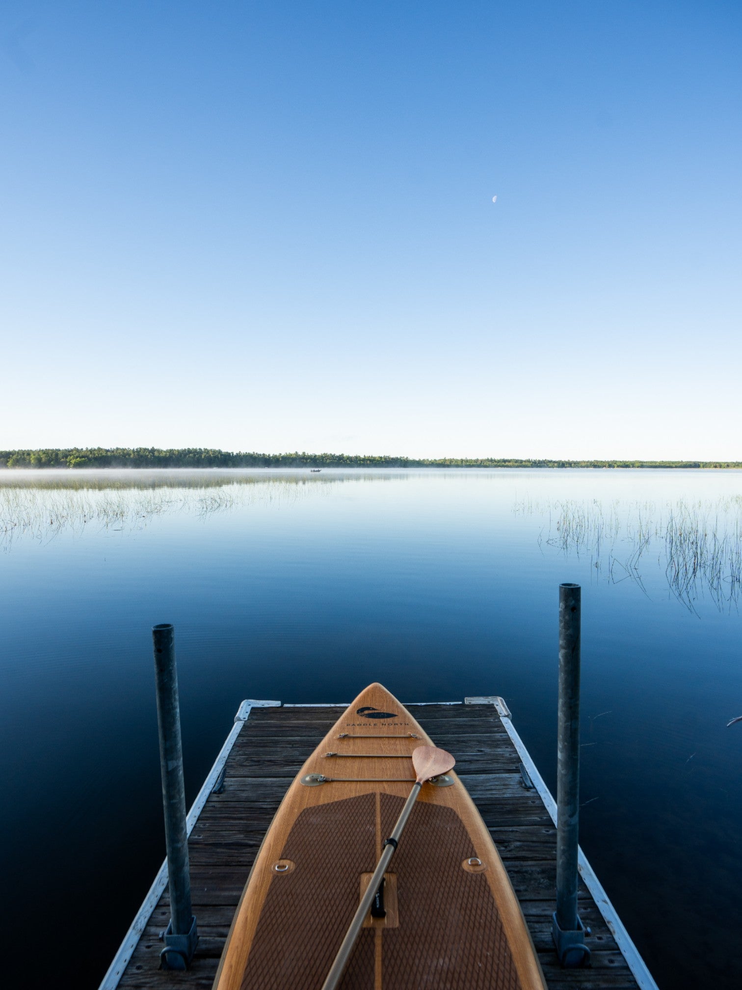 Paddle board sitting on a dock with a paddle resting on top.