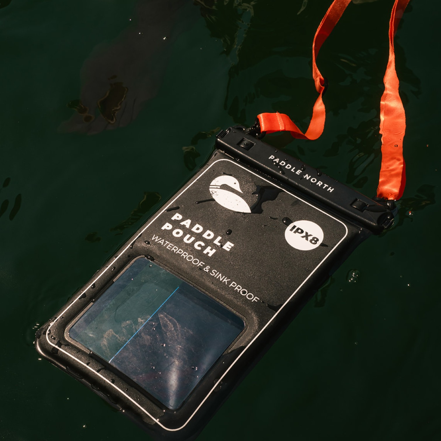 A black Paddle North waterproof pouch floating on the water.