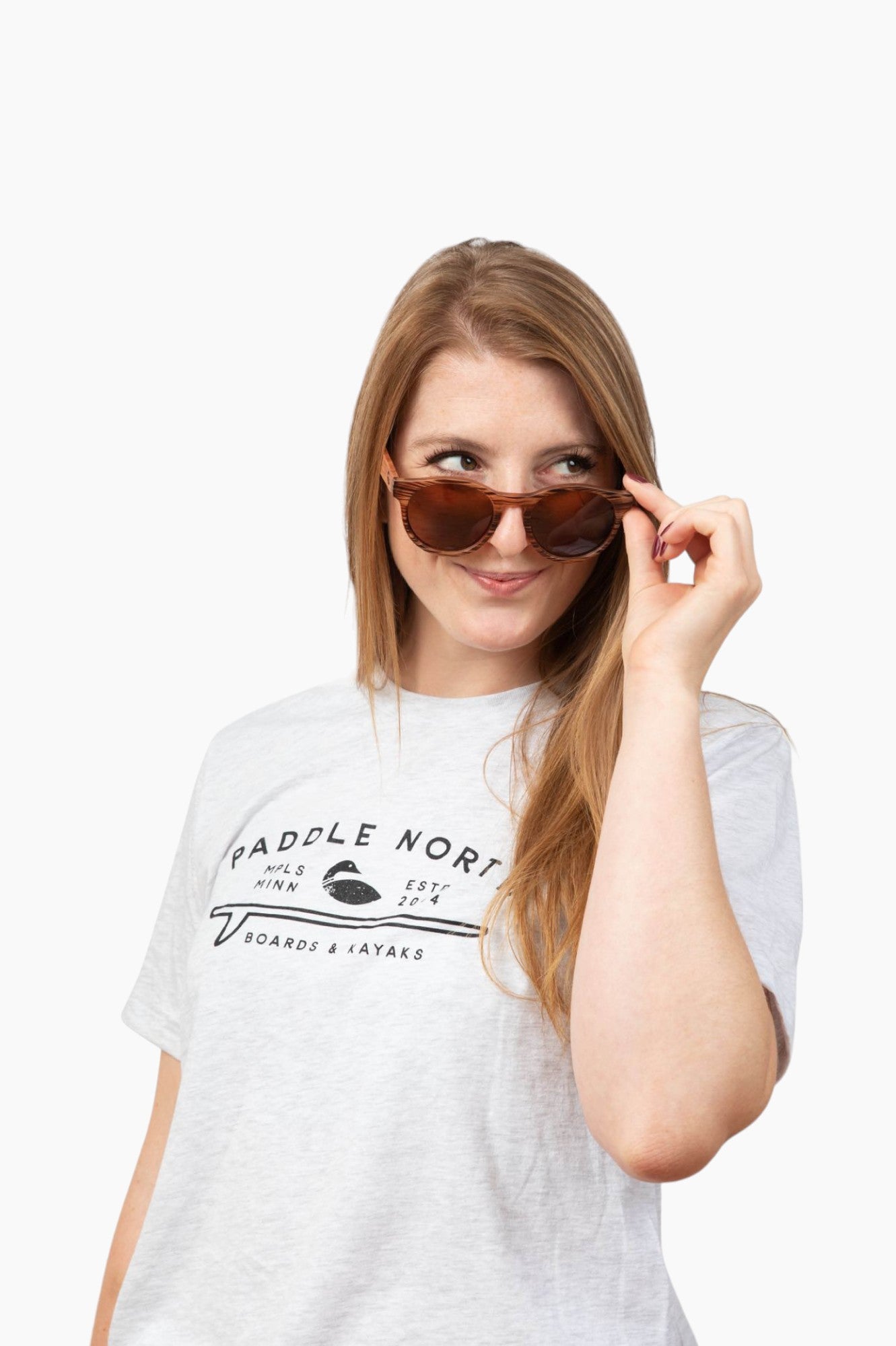 Woman wearing round, wood-looking framed sunglasses wearing a paddle north t-shirt.
