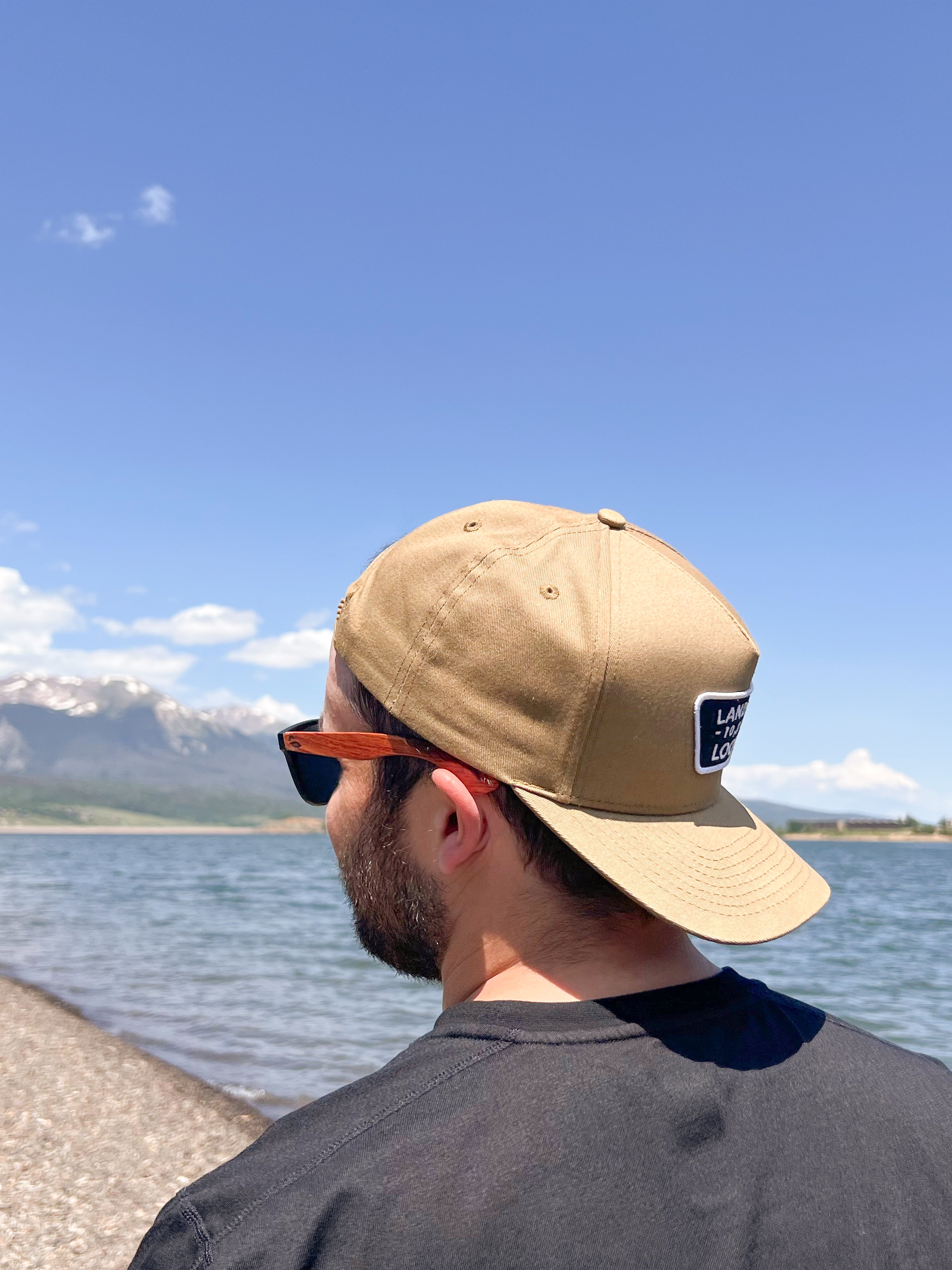 Man wearing hat backwards and sunnies looking off into the distance, showcasing the wooden sunglasses arms.