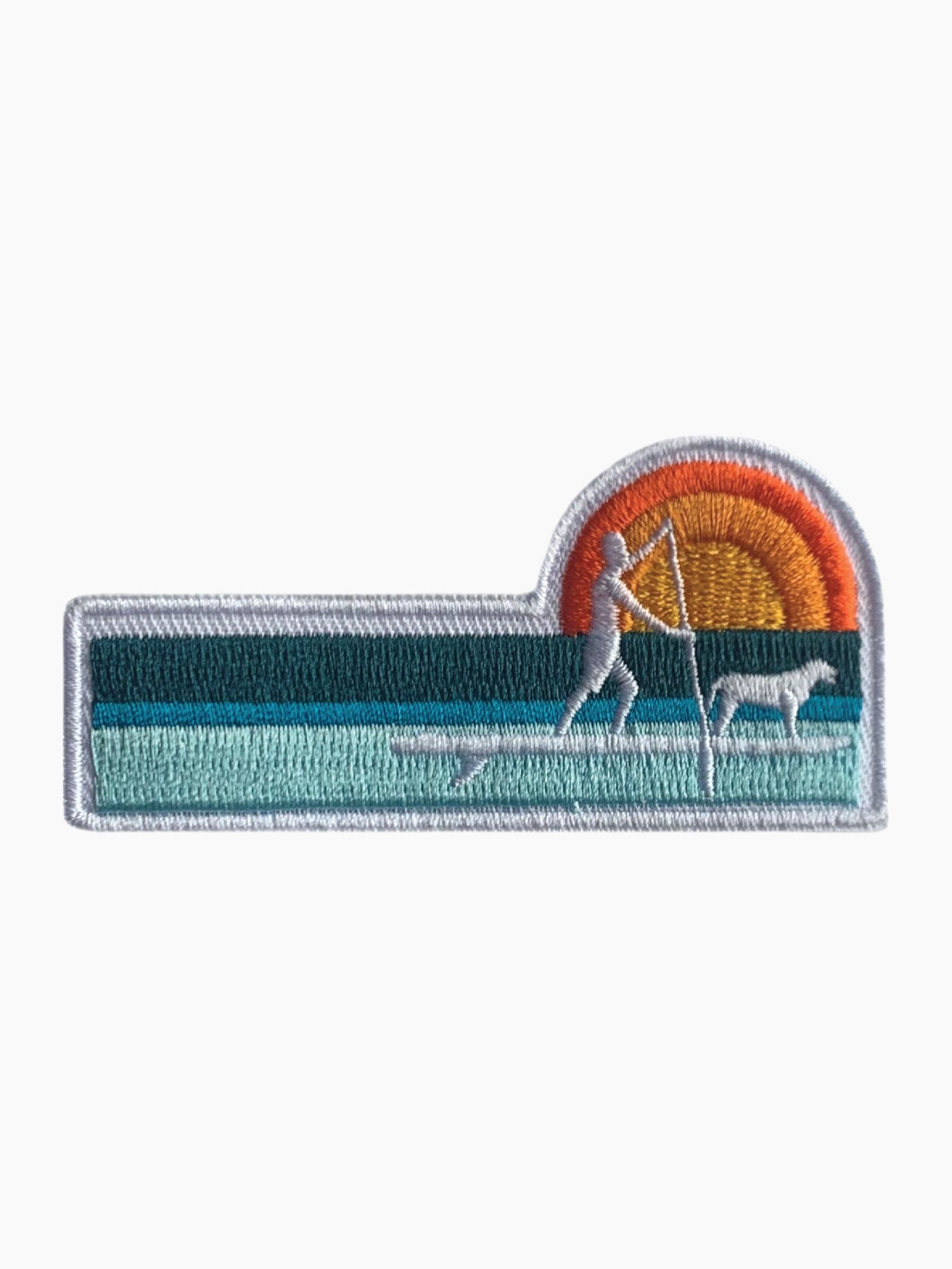 Woven badge with water lines, a sunset, and a person and dog on a paddle board.