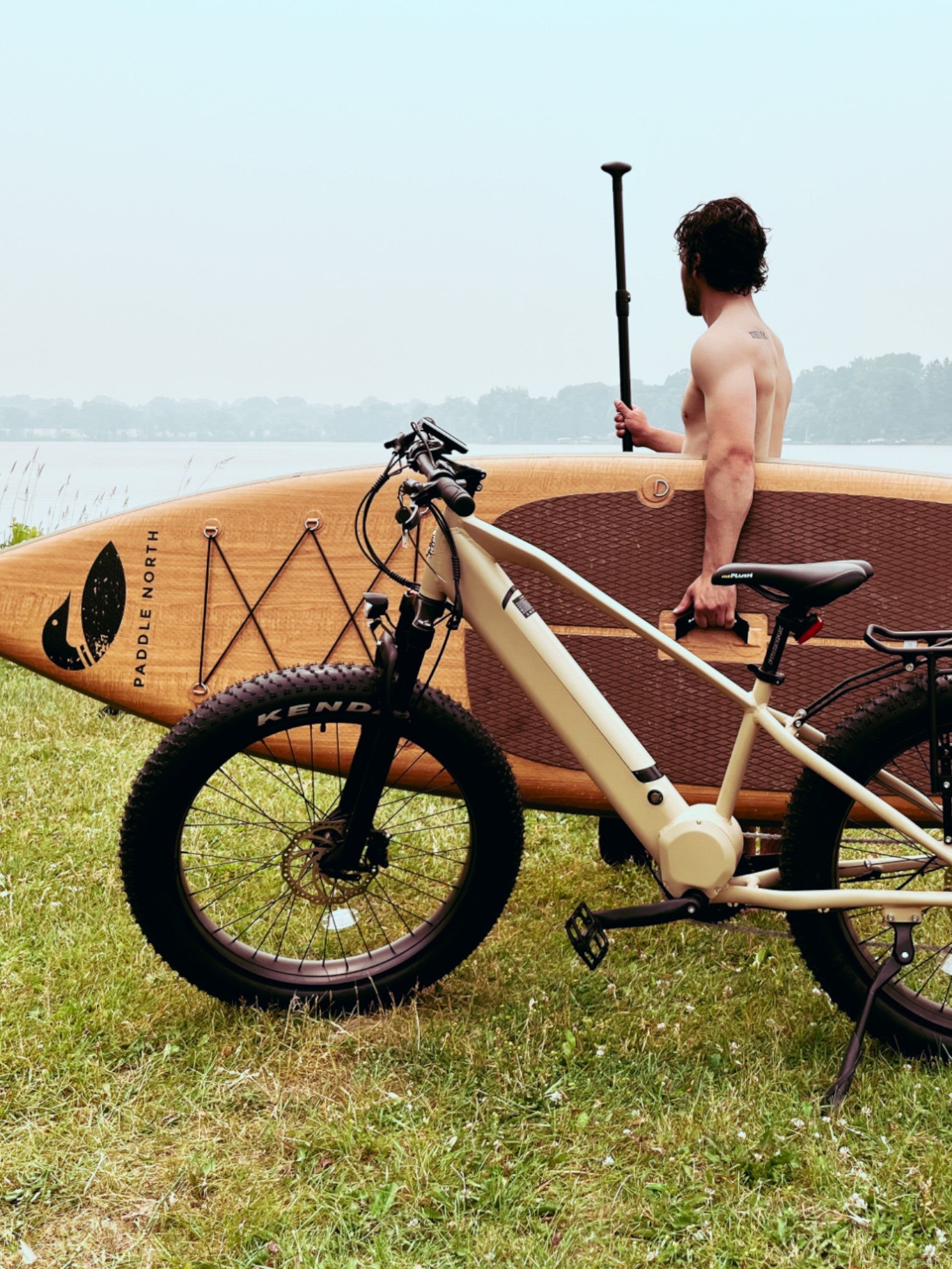 Parked tan electric bike in front of person holding an inflatable paddle board and paddle.