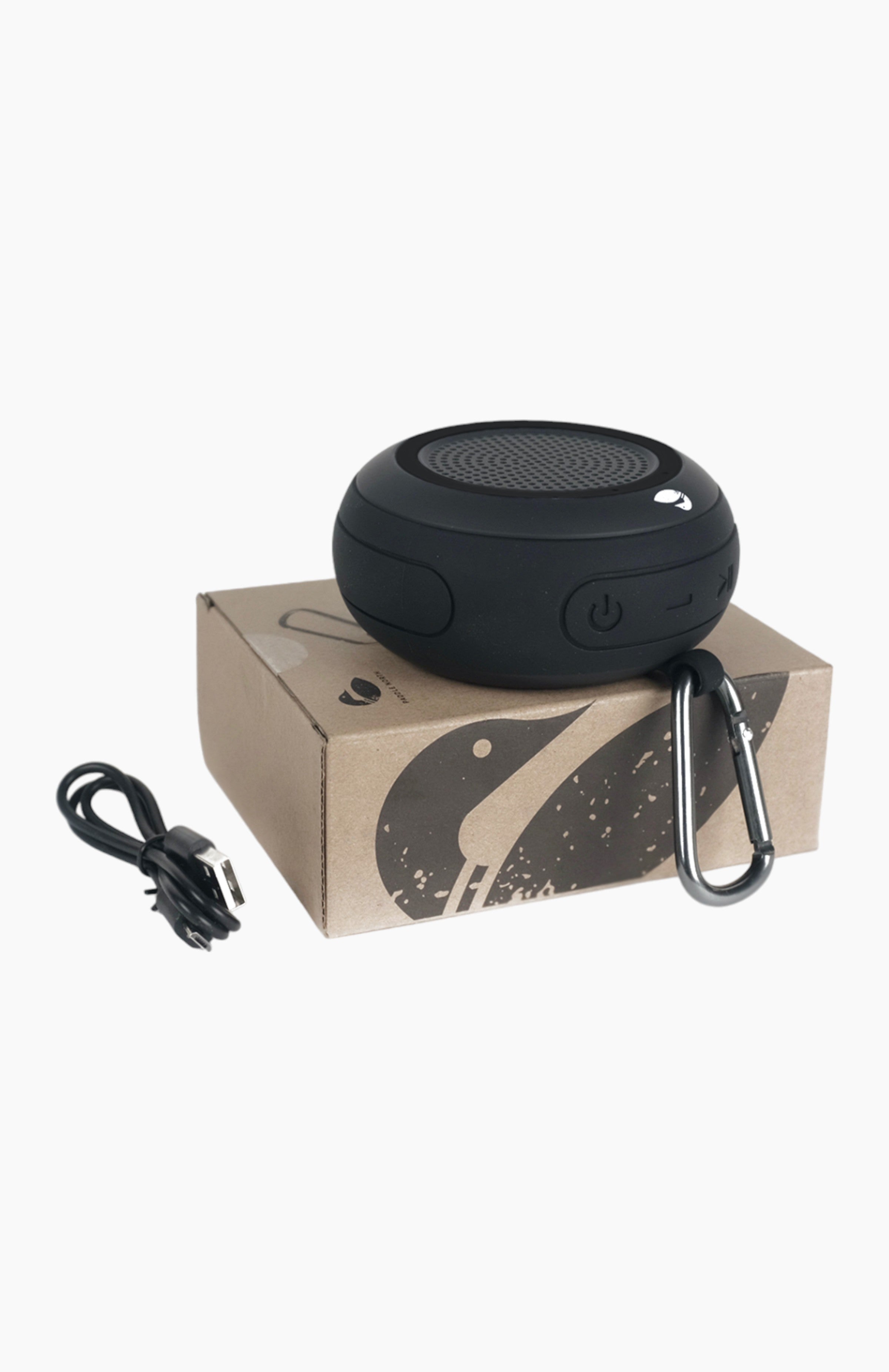 Black circular speaker sitting on top of it's box with it's charging chord.