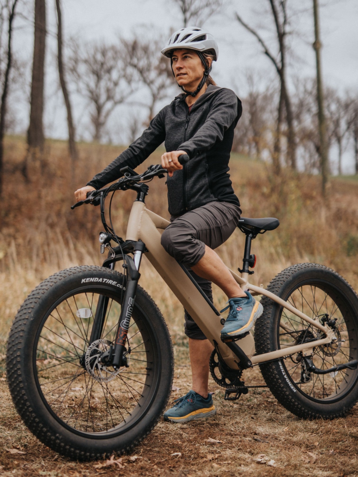 Person standing on their tan electric bike on a wooded trail.