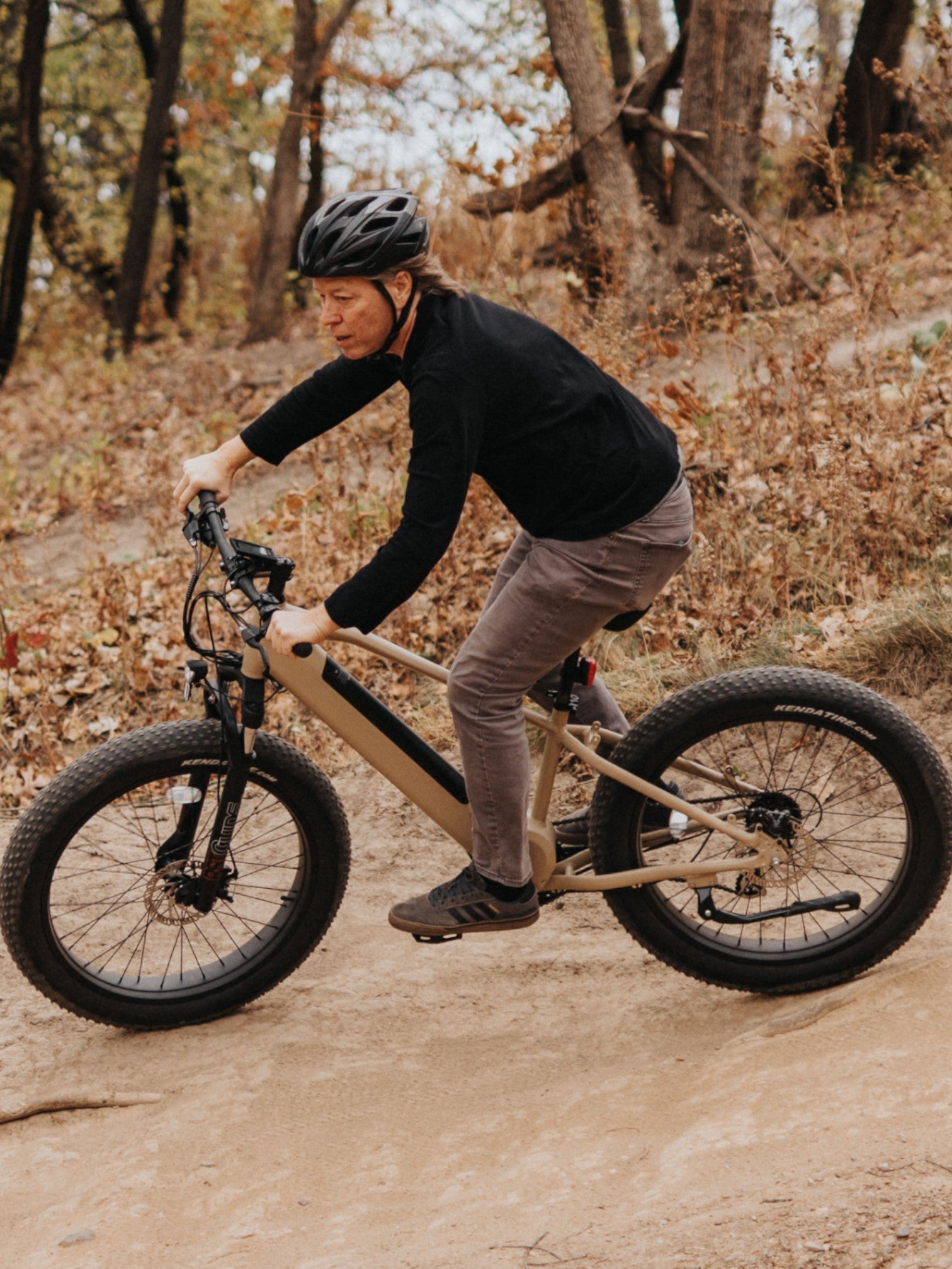 Person riding a tan electric bike on a wooded trail.