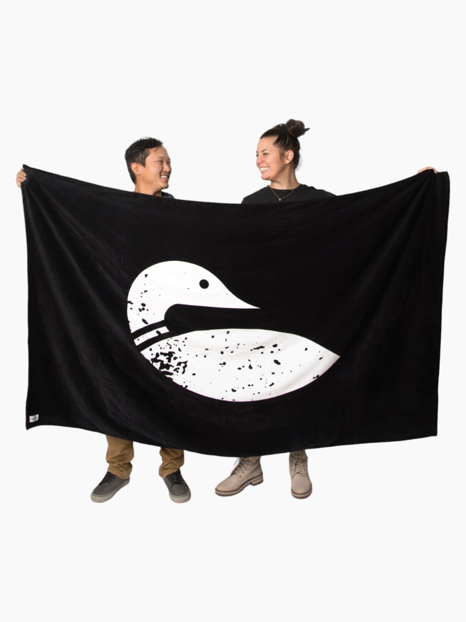 Lake accessories: Two people holding the black towel unrolled with the white paddle north loon logo on the front of it.